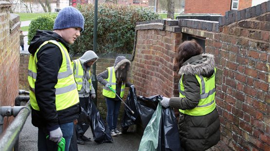 Students and staff picking up litter on a sloppy pathway near University of Worcester.