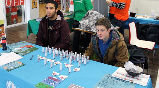 Two male students giving away poppy seeds in glass containers on a stall.