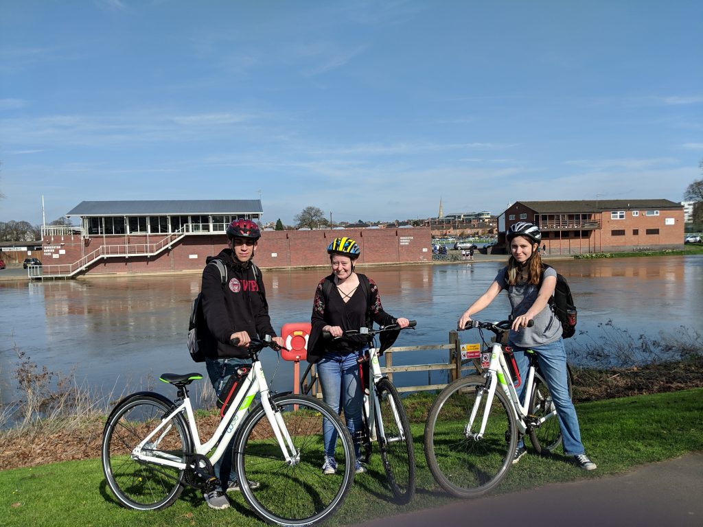 three students on bikes near the river in worcester