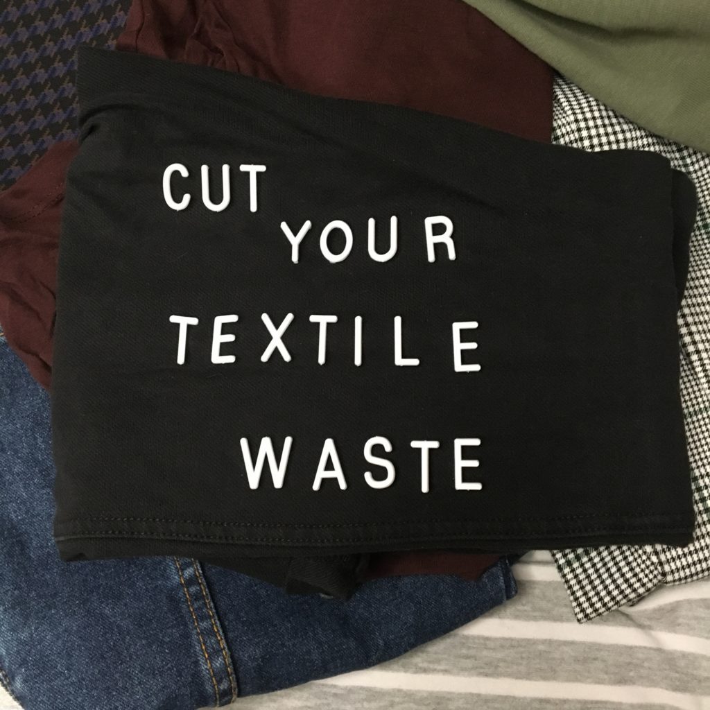 Pile of folded clothes with white text reading cut your textile waste