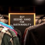 Clothes hanging in a wardrobe with a sign that reads 'buy second hand for sustainability'