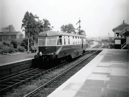 Black and white picture of a train on the track at a railway station.