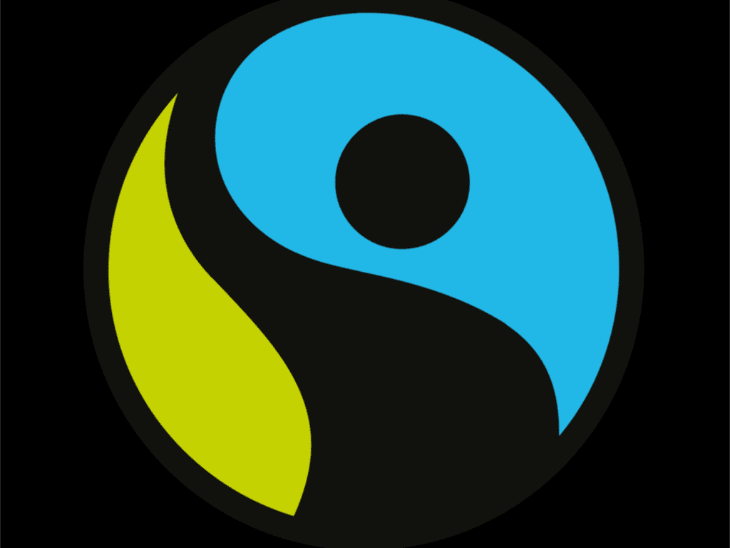 
The image shows the Fairtrade logo, which consists of a circular design split into two curved shapes resembling a yin-yang symbol. The left portion is green and the right portion is blue, with a small black circle in the blue section representing a person reaching upward. The background of the logo is black. This logo symbolizes ethical and sustainable trade practices, promoting fairness for producers.